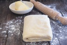 flour, butter and rolling pin sitting on a table next to a bowl with dough