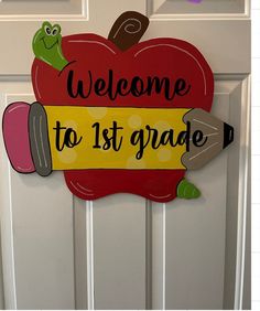 a welcome to 1st grade sign hanging on the front door with a pencil and apple