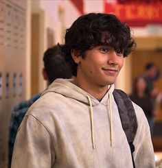 a young man with curly hair wearing a gray hoodie and smiling at the camera