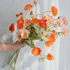 a person holding a bouquet of flowers on a white surface with orange and pink flowers