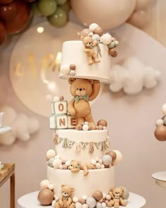 a teddy bear cake with balloons in the background and decorations around it for a baby's first birthday