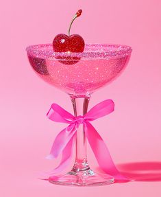 a pink martini glass with a cherry on the rim and a bow around the rim