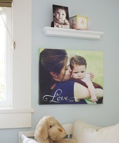 a baby's photo hangs on the wall next to a teddy bear and shelf