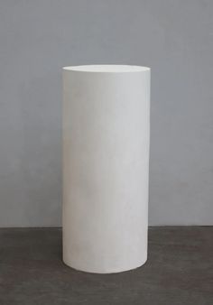 a tall white vase sitting on top of a cement floor next to a gray wall