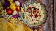 a bowl filled with mashed potatoes and bacon on top of a wooden table next to flowers