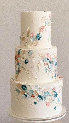 a three tiered white cake with blue and pink flowers on the top, sitting on a table