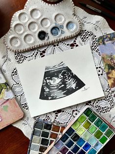 a table topped with lots of different types of paint and watercolors on top of a white doily