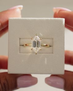 a woman's hand holding an engagement ring in a box