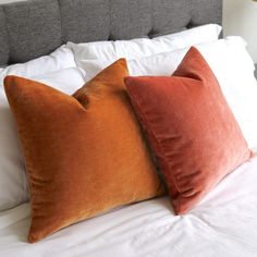 two orange and white pillows sitting on top of a bed next to a gray headboard