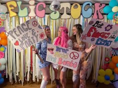 three women holding signs in front of a backdrop with balloons and streamers on it