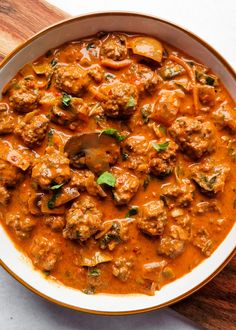 a white bowl filled with meatballs and sauce on top of a wooden cutting board