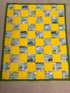 a yellow and blue quilt on the floor with a green border that has pictures of farm animals