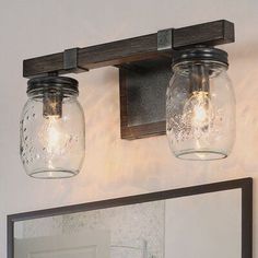 two mason jar lights are hanging on the wall above a mirror and vanity light fixture