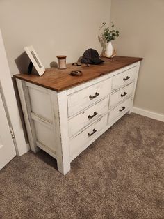 a white dresser with drawers and a hat on top, next to a door in a room