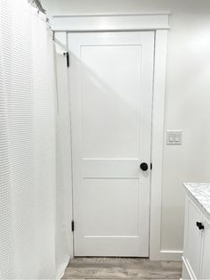 a white door in a bathroom next to a sink and shower curtain with black hardware