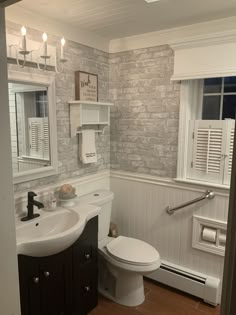 a white toilet sitting next to a sink in a bathroom under a window with shutters