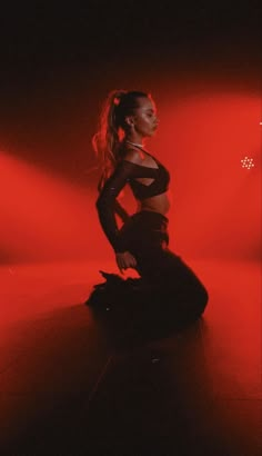 a woman sitting on the floor in a dark room with red light coming from behind her