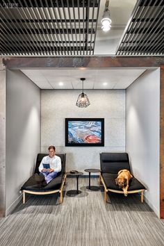 a man sitting in a room with two chairs and a dog standing next to him