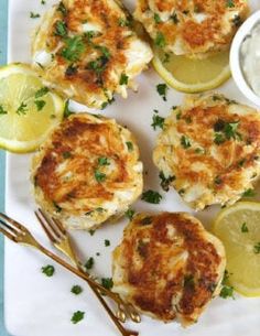 crab cakes with lemon wedges and tartar sauce on a white plate next to silverware