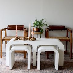 a white table with two benches and some candles on it in front of a plant