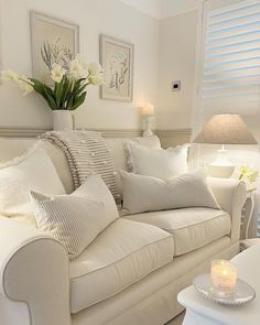 a living room with white furniture and flowers in vases on the coffee table next to the couch