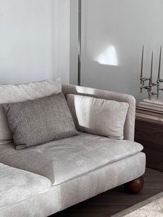 a white couch with pillows on top of it in front of a table and lamp