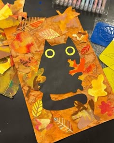 an art project made out of leaves and paper with a black cat on it's face