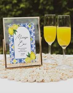 two glasses of orange juice are sitting on a table next to a sign that says lemon beer