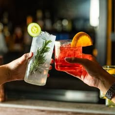 two people toasting with cocktails in front of them at a bar or restaurant