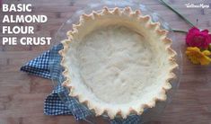 a pie crust sitting on top of a wooden table next to flowers and a blue checkered napkin