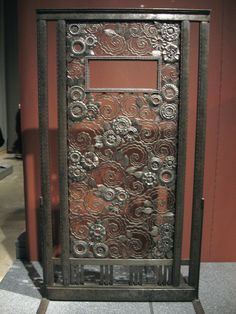 an ornate metal door is on display in a room with red walls and tile flooring