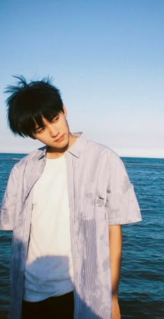 a young man standing in front of the ocean with his hair blowing in the wind