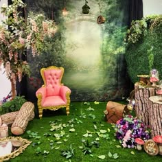 a pink chair sitting on top of a lush green field next to a forest backdrop