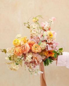 a person holding a bouquet of flowers in their hand with the background beige and white