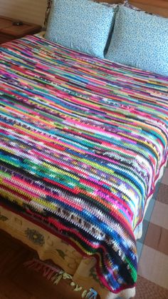 a bed with a colorful blanket on top of it next to a wooden headboard