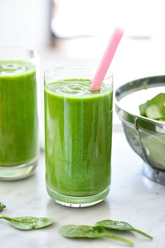 two glasses filled with green smoothie on top of a table