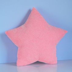 a pink star shaped pillow sitting on top of a white table next to a blue wall