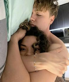 two people are cuddling in the middle of a bed with their arms around each other