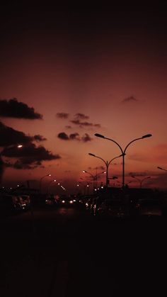 the sun is setting behind some street lights and cars on the road in front of them