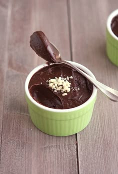 two green bowls filled with chocolate pudding on top of a wooden table next to spoons