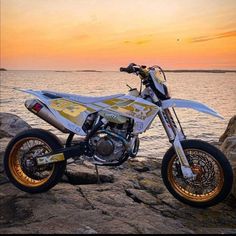 a white and yellow dirt bike parked on top of a rock next to the ocean