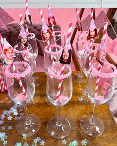 some wine glasses with pink and white striped straws in them on a wooden table