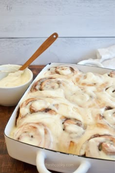 a casserole dish with cinnamon rolls and cream cheese sauce in the middle on a wooden table