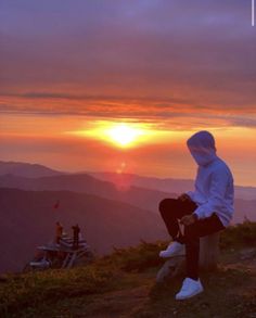 a person sitting on top of a hill with the sun setting in the distance behind them