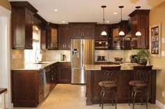 a large kitchen with wooden cabinets and stainless steel refrigerator freezer, oven, microwave, dishwasher and bar stools