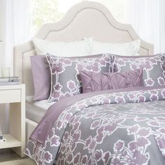 a bed with purple and white comforters in a bedroom next to a night stand