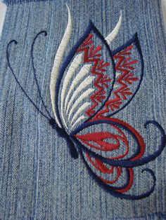 an embroidered butterfly is on the back of a pair of blue jean pants with red and white stitching