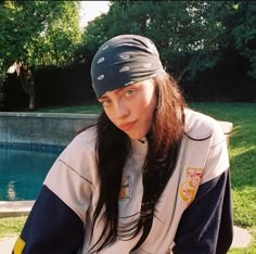 a woman sitting on top of a bench next to a swimming pool wearing a hat