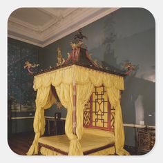 a canopy bed with yellow drapes and curtains on the sides, in a room with blue walls