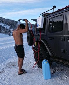 a man is washing his jeep in the snow with a water bottle and skis